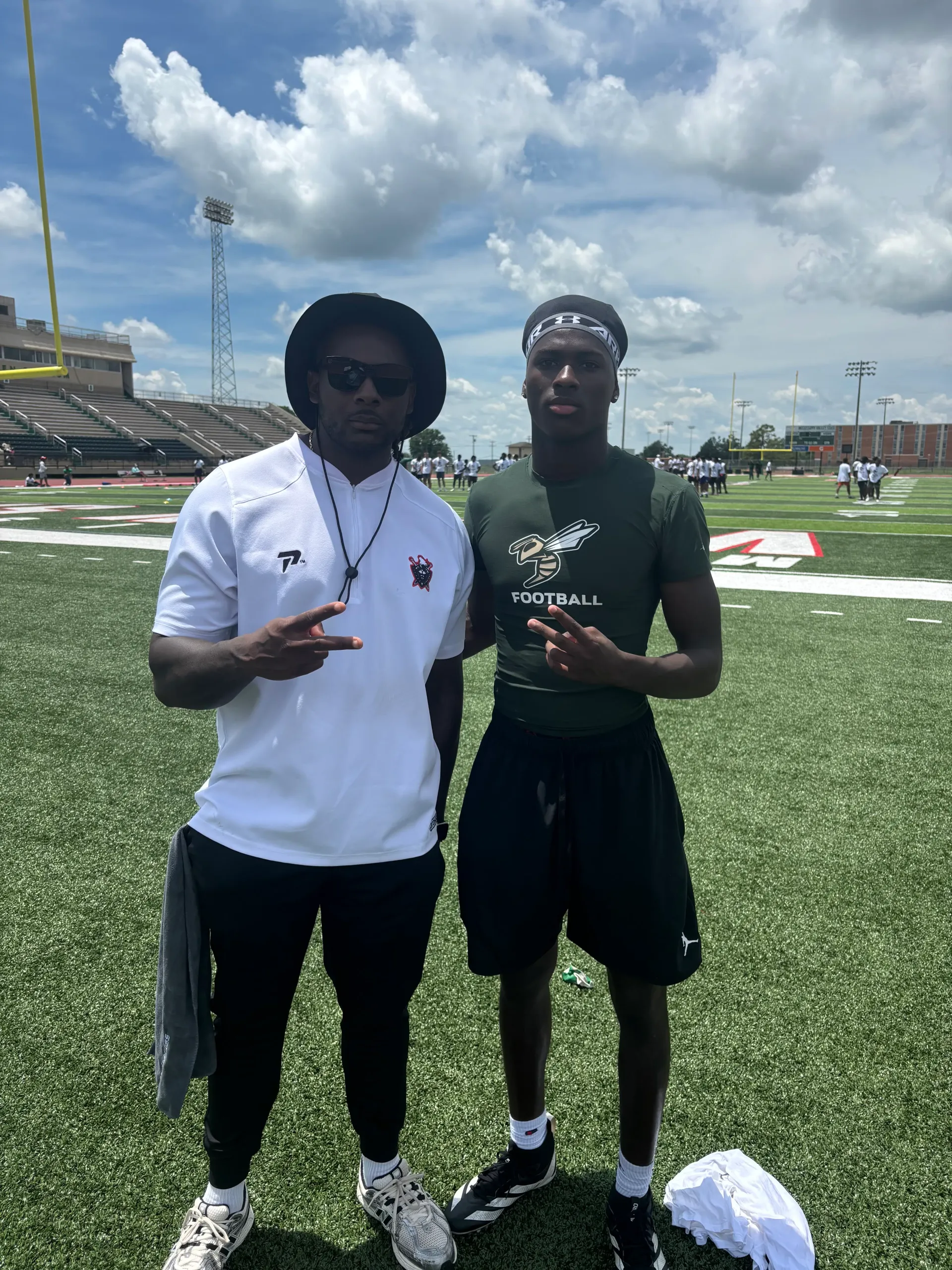 Coach Darnell Newman in a white coaching shirt standing with a recruit in a green football shirt on a sunny college football field