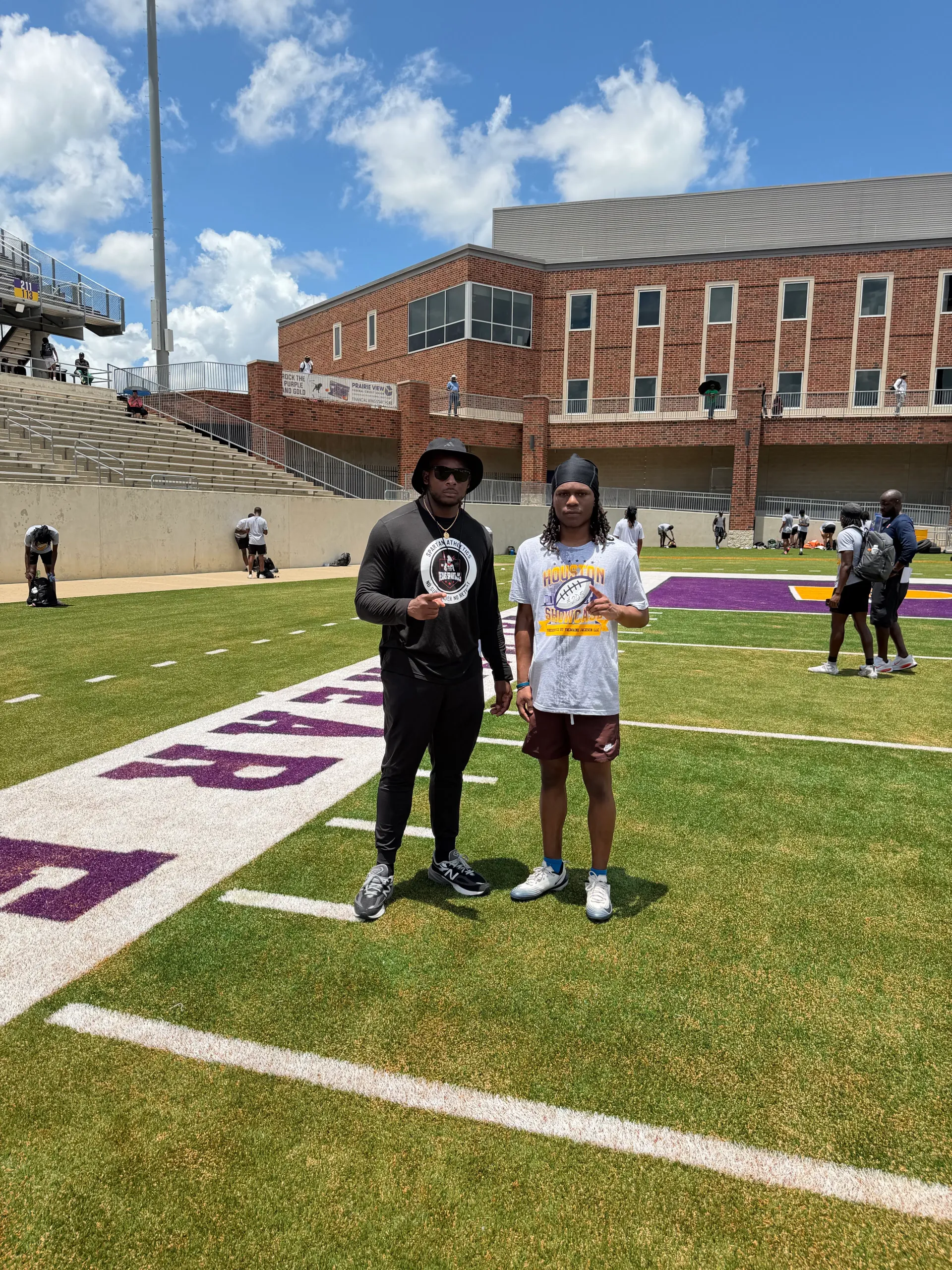 Coach Darnell Newman in a dark athletic top standing with a recruit on a purple and white college football field